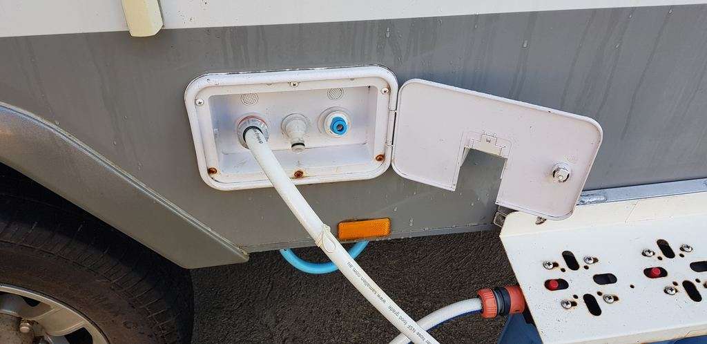 Caravan rainwater catchment filter hose on side of van filling tanks